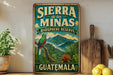 A vintage-style sign for the Sierra de las Minas Biosphere Reserve in Guatemala, featuring a colorful illustration of a bird perched on a tree branch with mountains in the background.