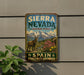 A vintage-style sign for Sierra Nevada Biosphere Reserve, featuring a mountain landscape with a goat and flowers, mounted on a wall next to a plant.
