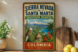 A vintage-style sign for Sierra Nevada de Santa Marta Biosphere Reserve in Colombia, featuring a tropical landscape with a bird, palm trees, and mountains.