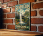 A vintage-style metal sign for Silver Falls State Park in Oregon, featuring a waterfall surrounded by lush greenery and flowers.