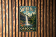 A vintage-style metal sign for Silver Falls State Park in Oregon, featuring a waterfall surrounded by lush greenery and flowers.
