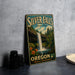 A vintage-style metal sign for Silver Falls State Park in Oregon, featuring a waterfall and lush greenery, is displayed on a gray countertop.