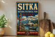 A vintage-style metal sign for Sitka National Historical Park in Alaska, featuring a scenic image of a mountain, a canoe, and traditional Alaskan architecture.