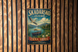 A vintage metal sign with a bird flying over a lake, surrounded by mountains, and a boat on the water. The sign is mounted on a wooden wall.