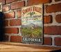 A vintage metal sign for Sonoma Valley, California, featuring a vineyard landscape and the text "Sonoma Valley Viticultural Heritage Landscape" against a brick wall background.