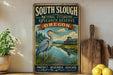 a vintage-style sign for the South Slough National Estuarine Research Reserve in Oregon, with a large blue heron in the foreground and a wooden paddle to the right.