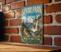 A vintage-style metal sign for the Spray Park Trail in Washington, featuring a scenic mountain landscape with a waterfall.
