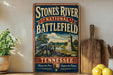 A vintage-style metal sign for the Stones River National Battlefield in Tennessee, featuring a cannon and a monument, is displayed on a shelf next to a wooden cutting board and a potted plant.