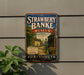 A vintage-style metal sign for the Strawberry Banke Museum, featuring a scenic illustration of a historic neighborhood with houses, trees, and a church.