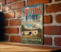 A vintage metal sign for Sutter's Fort, a State Historic Park in California, is displayed on a brick wall.
