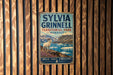 A vintage-style metal sign for Sylvia Grinnell Territorial Park in Nunavut, featuring a white goat on a rocky cliff overlooking a body of water.