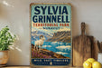 A vintage-style sign for Sylvia Grinnell Territorial Park in Nunavut, featuring a white ram standing on a rocky outcrop overlooking a body of water.