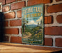A vintage-style metal sign for the Taconic Trail State Forest in Massachusetts, featuring a scenic illustration of a forest and mountains.