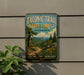 A vintage-style metal sign for the Taconic Trail State Forest in Massachusetts, featuring a scenic landscape with pine trees, mountains, and a winding path.