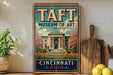 A vintage-style metal sign for the Taft Museum of Art in Cincinnati, Ohio, featuring an illustration of the museum building surrounded by flowers and trees.