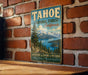 A vintage-style metal sign for Tahoe National Forest in California, featuring a scenic landscape with mountains, pine trees, and a lake.