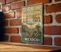 A vintage-style metal sign with text and illustrations of a desert landscape, mounted on a brick wall.