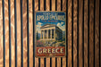 A vintage metal sign displaying the Temple of Apollo Epicyclus at Bassae, with the text "TEMPLE OF APOLLO EPICURIUS AT BASSAE" and "GREECE" below the image of the temple.