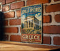 A vintage metal sign displaying the Temple of Apollo Epicyclus at Bassae, a landmark in Greece, mounted on a brick wall.