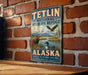 A vintage-style metal sign for the Teltlin National Wildlife Refuge in Alaska, featuring an illustration of wildlife such as a moose, eagle, and loon.