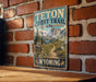A vintage-style metal sign for the Teton Crest Trail in Wyoming, featuring a scenic mountain landscape and trail map.