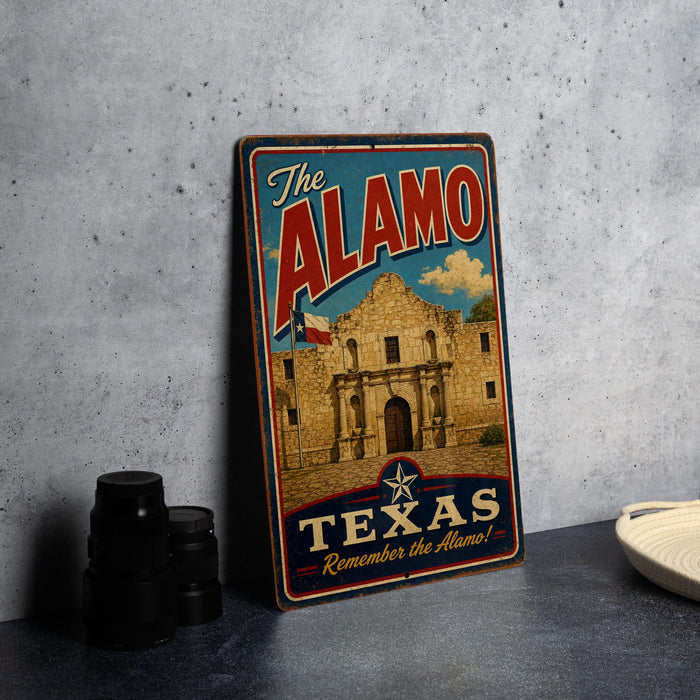 A vintage-style metal sign with the text "The Alamo" and "Texas" printed on it, featuring an illustration of the Alamo building.