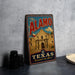 A vintage-style metal sign with the text "The Alamo" and "Texas" printed on it, featuring an illustration of the Alamo building.
