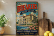 A vintage-style metal sign for "The Breakers" in Rhode Island, featuring an illustration of a grand mansion with a river and flowers in the foreground.