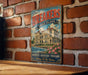 A vintage metal sign for "The Breakers" in Rhode Island, featuring an illustration of a building and a river, mounted on a brick wall.