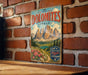 A vintage metal sign with a mountain landscape and flowers is hanging on a brick wall.