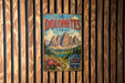 A vintage metal sign with the text "The Dolomites Italy" and a mountain landscape illustration is displayed on a wooden wall.