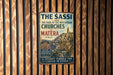 A vintage metal sign with text and an illustration of a cityscape, mounted on a wooden wall.