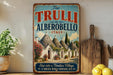 a vintage-style sign for "The Trulli of Alberobello, Italy", depicting a picturesque village with white buildings and colorful roofs.