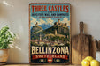 A vintage-style metal sign with the text "Three Castles and Defensive Wall and Ramparts of the Market-Town of Bellinzona Switzerland" displayed on a shelf.