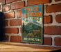 A vintage-style metal sign for Tiger Mountain State Forest in Washington, featuring a mountain landscape and a sign indicating the location.