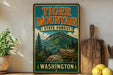 A vintage-style sign for Tiger Mountain State Forest in Washington, featuring a mountain landscape and a wooden sign with the text "Tiger Mountain Elev. 8,015 ft".