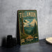 A vintage-style metal sign for Tillamook State Forest, featuring a scenic mountain landscape and a road leading through the forest.