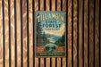 A vintage metal sign for Tillamook State Forest in Oregon, featuring a scenic illustration of the forest and mountains.