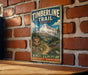 A vintage-style metal sign for the Timberline Trail in Oregon, featuring a mountain landscape and trail marker.