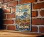 A vintage-style metal sign with the text "Tombstone Territorial Park Yukon Canada's True North" is displayed on a brick wall.