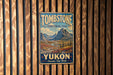 A vintage-style sign for Tombstone Territorial Park, featuring a scenic mountain landscape with a river and pine trees.