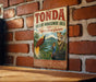 A vintage-style metal sign for the Tonda Wildlife Management Area in Papua New Guinea, featuring illustrations of various animals such as a parrot, a bird, and a kangaroo.