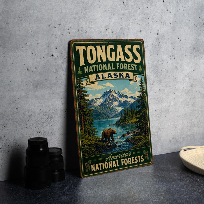 A vintage-style metal sign for Tongass National Forest in Alaska, featuring a scenic illustration of a bear in the foreground with mountains and a river in the background.