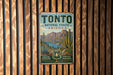 A vintage metal sign for Tonto National Forest in Arizona, featuring a scenic landscape with mountains, cacti, and a lake.