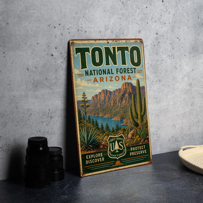 A vintage-style sign for the Tonto National Forest in Arizona, featuring a desert landscape with mountains, cacti, and a lake.