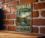 A vintage-style metal sign for the Topmead State Forest in Connecticut, featuring a scenic landscape with a river and a bridge.