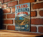 A vintage metal sign for the Trans-Catalina Trail in Catalina Island, California, featuring a scenic mountain landscape and directional signs.