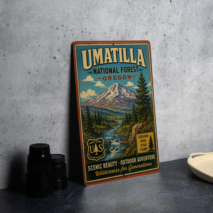 A vintage-style metal sign for the Umatilla National Forest in Oregon, featuring a scenic mountain landscape and text promoting outdoor adventure and wilderness.