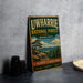 A vintage-style metal sign for Uwharrie National Forest, featuring a scenic landscape with a pine tree and mountains, is displayed on a gray countertop next to some black camera lenses.