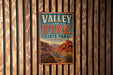 A vintage metal sign for Valley of Fire State Park in Nevada, featuring a desert landscape with mountains and a winding road.
